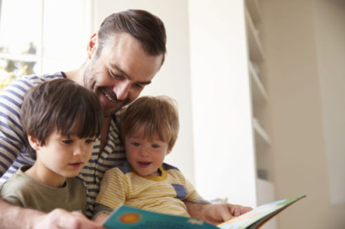 Close Up Of Father And Sons Reading Story At Home